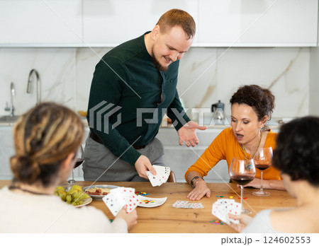 Friendly company of men and women sitting at kitchen table and enjoying the poker game. Friends play a card game at home. Evening entertainment concept 124602553