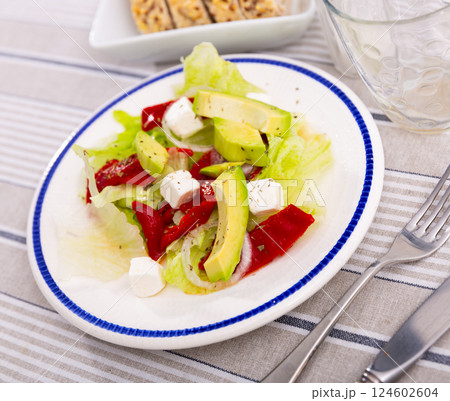 Salad with avocado, peppers, cheese and onions on a white plate 124602604