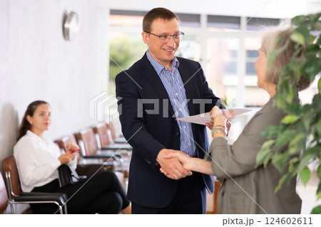 Senior woman makes deal, shaking hands with middle-aged man colleague while standing in office 124602611