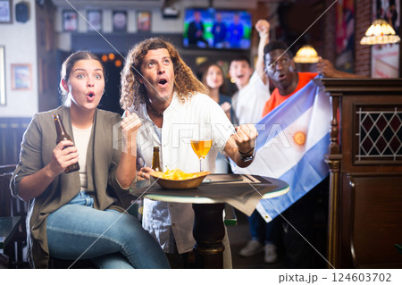Expressive couple drinking beer and rooting for favorite Argentinean team in sports bar Expressive couple drinking beer and rooting for favorite Argentinean team in sports bar 124603702
