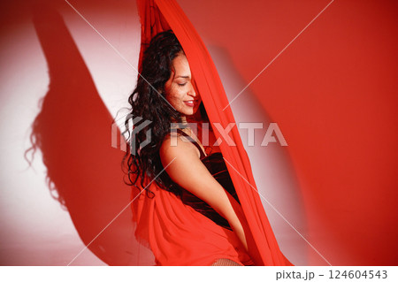 Curly brunette girl posing for a photo. Girl wearing velour bodysuit and is wrapped in red scarf. Projectors light girl up. 124604543