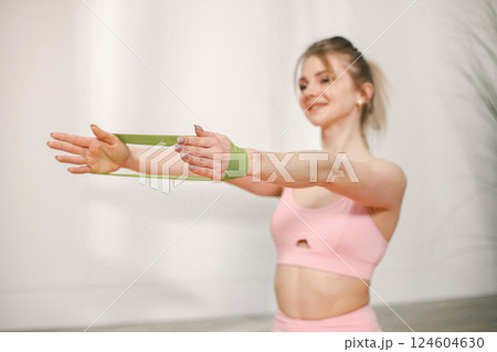 Cropped photo of sporty young woman training with elastic rope at home. Woman wearing rose top and leggins. Portrait of a woman doing exercises. 124604630