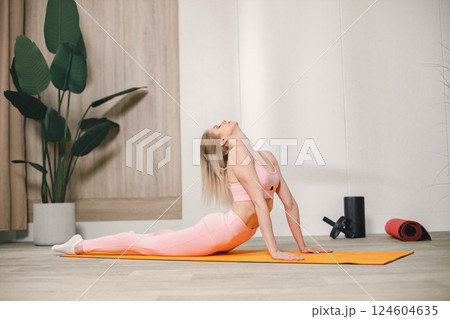 Sporty young woman training at home. Woman wearing rose top and leggins. Woman doing yoga on an orange mat. 124604635