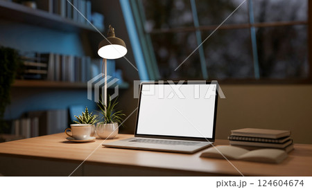 The white screen laptop on wooden table with decors placing under the roof window in the dark room. The white screen laptop on wooden table with decors placing under the roof window in the dark room. 124604674