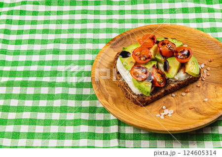 Avocado and tomato toast on a wood plate with a green checkered cloth 124605314