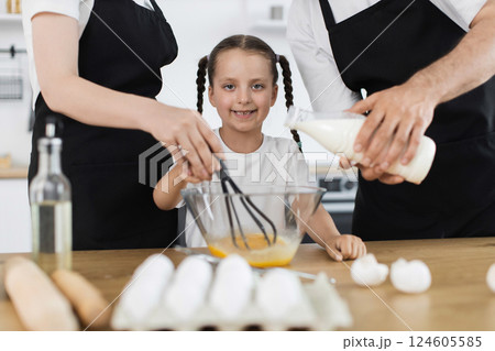Caucasian family in kitchen preparing ingredients, young girl happily using whisk to mix. 124605585