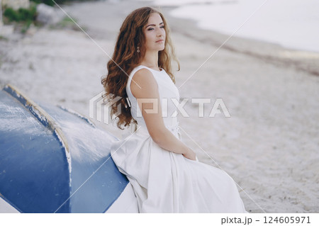 Beautiful long-haired bride in a magnificent white dress sitting near boat Beautiful long-haired bride in a magnificent white dress sitting near boat 124605971