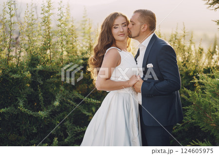 beautiful long-haired bride in white dress with her young man walking in the nature 124605975