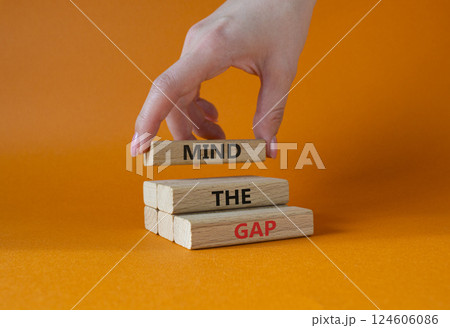 Mind the gap symbol. Concept words Mind the gap on wooden blocks. Beautiful orange background. Businessman hand. Business and Mind the gap concept. Copy space. 124606086
