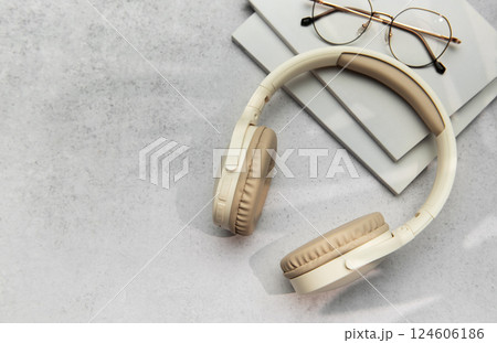 Modern wireless headphones lying on table next to books and eyeglasses 124606186