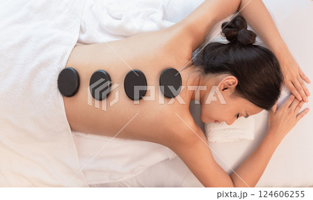 Beautiful young woman relaxing in spa salon with hot stone massage on body. Beauty treatment therapy 124606255
