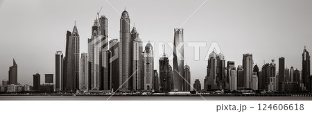 Monochrome city skyline with tall skyscrapers reflecting on calm water under a cloudy sky, Dubai Marina bay UAE 124606618