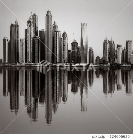 Monochrome city skyline with tall skyscrapers reflecting on calm water under a cloudy sky, Dubai Marina bay UAE Monochrome city skyline with tall skyscrapers reflecting on calm water under a cloudy sky, Dubai Marina bay UAE 124606620