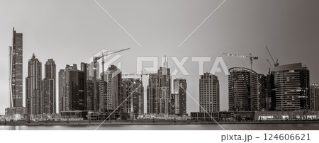 Monochrome city skyline with tall skyscrapers reflecting on calm water under a cloudy sky, Dubai Marina bay UAE Monochrome city skyline with tall skyscrapers reflecting on calm water under a cloudy sky, Dubai Marina bay UAE 124606621