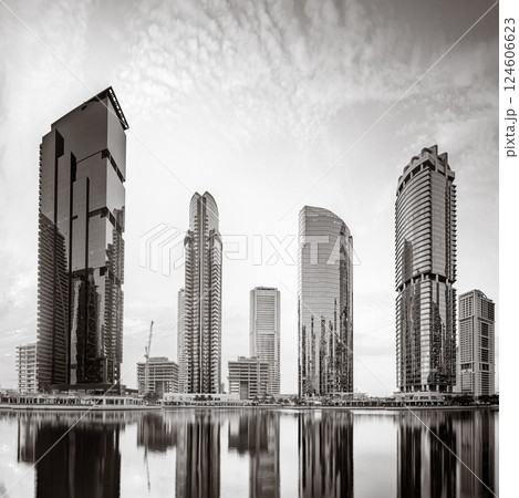 Monochrome city skyline with tall skyscrapers reflecting on calm water under a cloudy sky, Dubai Marina bay UAE Monochrome city skyline with tall skyscrapers reflecting on calm water under a cloudy sky, Dubai Marina bay UAE 124606623