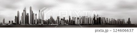 Monochrome city skyline with tall skyscrapers reflecting on calm water under a cloudy sky, Dubai Marina bay UAE 124606637