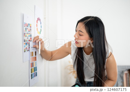 An asian woman is sticking a printed color palette or a color chart on the wall. Designer at work. 124607175
