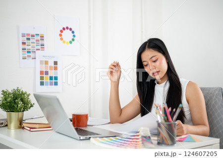 Asian woman is reading the documents while making a design on a graphic tablet and a laptop. Asian woman is reading the documents while making a design on a graphic tablet and a laptop. 124607205