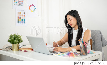 Asian woman is drawing or making a design on a graphic tablet and pressing a key on laptop keyboard 124607207
