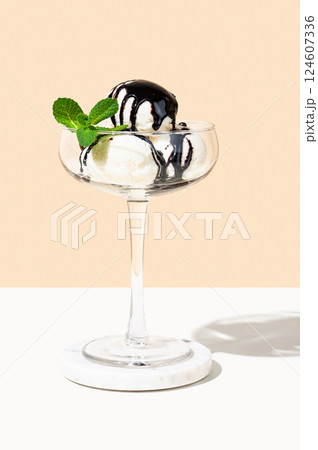 Scoops of vanilla ice cream in a tall glass with chocolate topping and a mint leaf  124607336