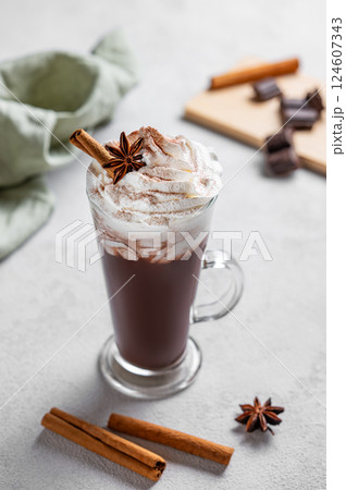 Hot chocolate with whipped cream, cinnamon and spices in a tall glass on a light background  124607343