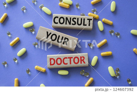 Consult Your Doctor symbol. Concept word Consult Your Doctor on wooden blocks. Beautiful purple background with pills. Medicine and Consult Your Doctor concept. Copy space 124607392