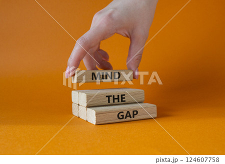 Mind the gap symbol. Concept words Mind the gap on wooden blocks. Beautiful orange background. Businessman hand. Business and Mind the gap concept. Copy space. 124607758