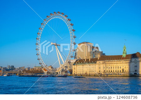 The London Eye stands tall against a clear blue sky, offering breathtaking panoramas of the River Thames and iconic London architecture. Visitors enjoy a memorable observation experience. 124608736