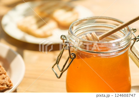 A Jar of Honey Sits in a Warm, Sunlit Kitchen With a Wooden Dipper Resting Inside A Jar of Honey Sits in a Warm, Sunlit Kitchen With a Wooden Dipper Resting Inside 124608747