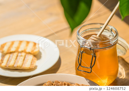 Honey Jar and Wooden Dipper With Grilled Bread Slices on a Sunny Table, Perfect for Food Bloggers and Enthusiasts Honey Jar and Wooden Dipper With Grilled Bread Slices on a Sunny Table, Perfect for Food Bloggers and Enthusiasts 124608752