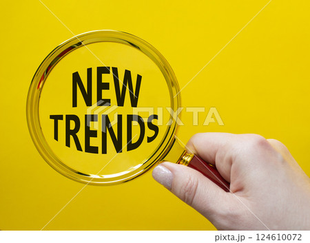New Trends symbol. Magnifying glass with words New Trends. Businessman hand. Beautiful yellow background. Business and New Trends concept. Copy space. 124610072