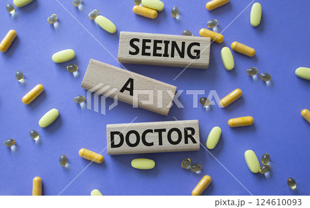 Seeing a Doctor symbol. Concept word Seeing a Doctor on wooden blocks. Beautiful purple background with pills. Medicine and Seeing a Doctor concept. Copy space Seeing a Doctor symbol. Concept word Seeing a Doctor on wooden blocks. Beautiful purple background with pills. Medicine and Seeing a Doctor concept. Copy space 124610093