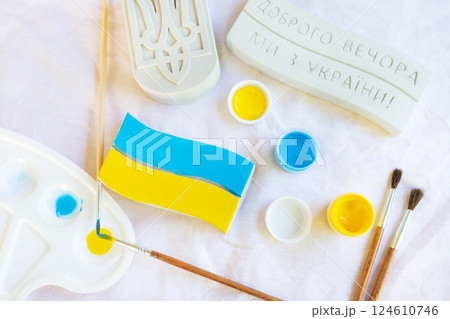 Artistic process of painting the Ukrainian flag with blue and yellow colors using brushes and paint palette 124610746