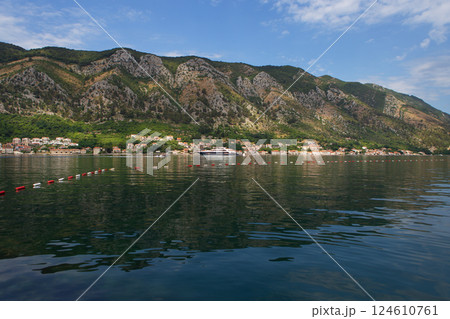 A picturesque coastal town nestled against a dramatic mountain range, with a large yacht in the calm waters 124610761