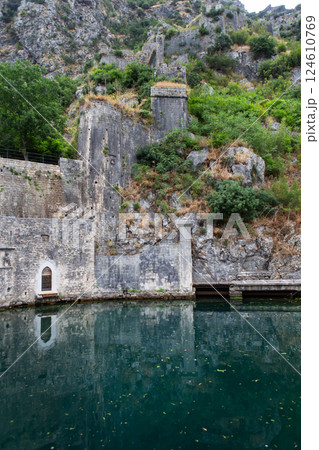 Ancient stone fortress walls and towers cling dramatically to a steep, rocky hillside overlooking calm water Ancient stone fortress walls and towers cling dramatically to a steep, rocky hillside overlooking calm water 124610769