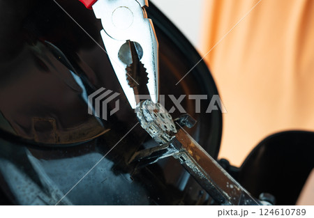 A close-up shot shows a person using pliers to carefully remove a small, dusty part from a broken appliance A close-up shot shows a person using pliers to carefully remove a small, dusty part from a broken appliance 124610789