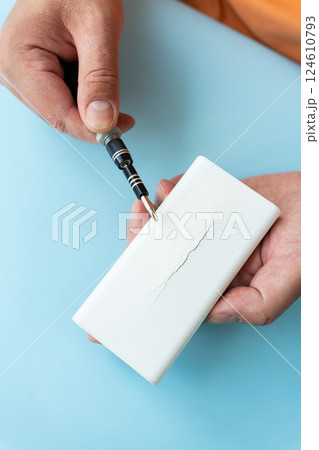 A person carefully uses a small screwdriver near a cracked white device 124610793