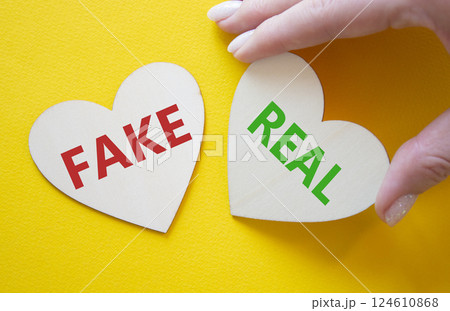 Real or Fake symbol. Concept word Real or Fake on wooden hearts. Businessman hand. Beautiful yellow background. Business and Real or Fake concept. Copy space Real or Fake symbol. Concept word Real or Fake on wooden hearts. Businessman hand. Beautiful yellow background. Business and Real or Fake concept. Copy space 124610868