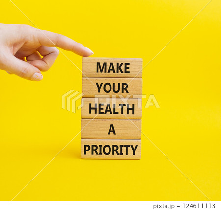 Health symbol. Wooden blocks with words Make your health a Priority. Businessman hand. Beautiful yellow background. Health concept. Copy space. Health symbol. Wooden blocks with words Make your health a Priority. Businessman hand. Beautiful yellow background. Health concept. Copy space. 124611113