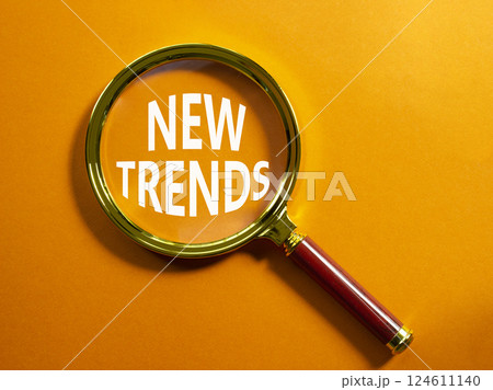 New Trends symbol. Magnifying glass with words New Trends. Beautiful orange background. Business and New Trends concept. Copy space. 124611140