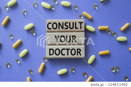 Consult Your Doctor symbol. Concept word Consult Your Doctor on wooden blocks. Beautiful purple background with pills. Medicine and Consult Your Doctor concept. Copy space 124611492