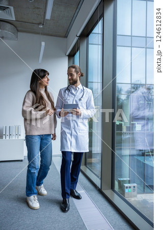 Doctor in hospital corridor guiding patient with tablet for digital consultation Doctor in hospital corridor guiding patient with tablet for digital consultation 124612834