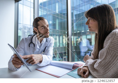 Surgeon in hospital using digital tablet discussing healthcare procedures with patient 124612857