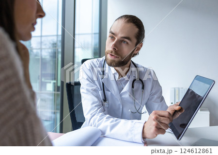 Surgeon in hospital using digital tablet discussing healthcare procedures with patient 124612861