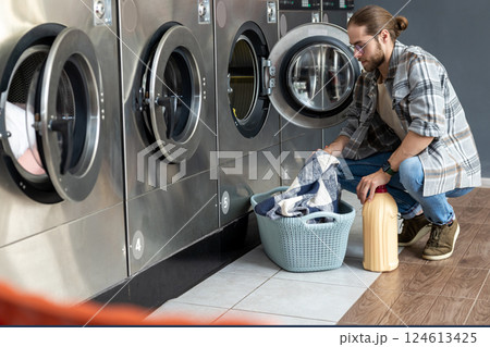 Adult man in self-service laundry shop operating coin washing machine Adult man in self-service laundry shop operating coin washing machine 124613425