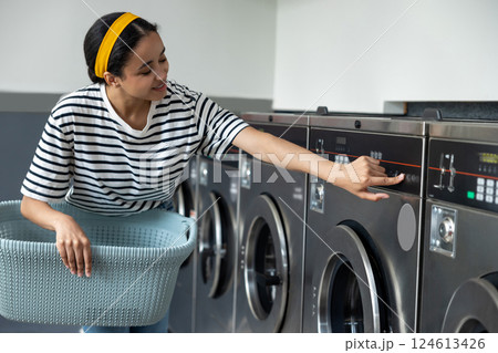 Female in launderette using industrial washer pushes a button to switch on 124613426