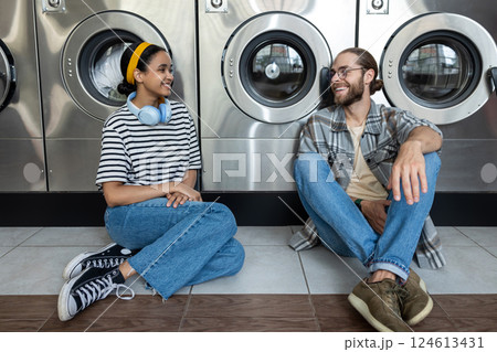 Couple in public laundromat talking while waiting for washing machine to finish their laundry chore 124613431