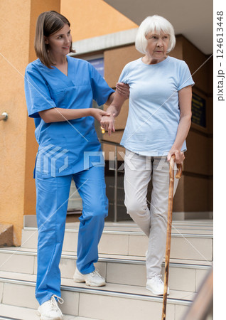 Female nurse walking with elderly patient supporting to retiree Female nurse walking with elderly patient supporting to retiree 124613448