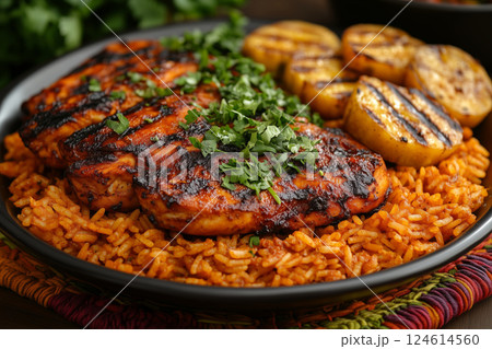 a traditional African meal featuring jollof rice, served with grilled chicken and fried plantains, garnished with fresh herbs, set on a colorful woven mat under natural daylight 124614560