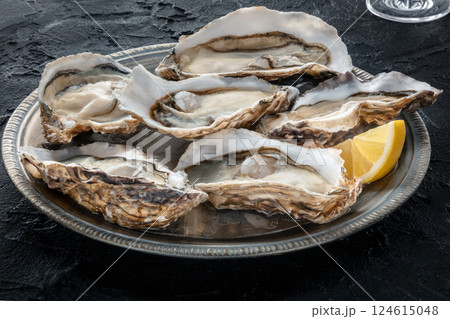 Fresh raw oysters on ice with lemon, on a black stone table 124615048